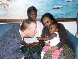 In a lighthearted moment, Holy Family Shelter director Bill Bickel, left, pretends to take a cracker from Tonika Mitchum, the 1-year-old daughter of Jolanda Mitchum, second from left. Tonika and Jolanda reside at the shelter. Tonika is being held by Nigisty Christos, Bickel&rsquo;s administrative assistant.