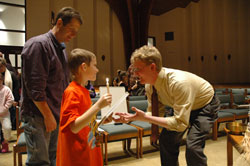 David Ballintyn gives a first Communion textbook to Aaron Adrian, a second-grader at St. Mark School, during a Jan. 9 meeting at St. Mark the Evangelist Church in Indianapolis. Aaron&rsquo;s father, Anthony Adrian, stands behind him.