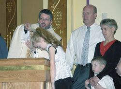 Father Christopher Craig, pastor of St. Mary of the Immaculate Conception Parish in Aurora, baptizes Molly Schmahl during the parish&rsquo;s Easter Vigil on April 7. Molly&rsquo;s parents, Kurt and April Schmahl, and her younger brother, Noah, look on. Kurt, Noah, and two of Molly&rsquo;s older sisters were also received into the Church during the liturgy. (Submitted photo) 