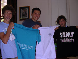 Members of the SMOKN&rsquo; Youth Ministry of St. Mary-of-the-Knobs Parish in Floyds Knobs and St. Mary Parish in Navilleton display a few of the T-shirts they will trade with &ldquo;One Bread, One Cup&rdquo; participants from other communities. From left are Matthew Hamilton, Paul Crockett and Kevin Crockett, all members of St. Mary-of-the-Knobs Parish. Their group&rsquo;s slogan is &ldquo;We&rsquo;re fired up for Jesus.&rdquo; (Photo by Patricia Happel Cornwell) 