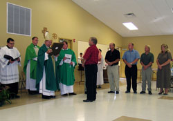 Archbishop Daniel M. Buechlein is presented with a plaque during the Sept. 16 dedication of the new parish life center at St. John the Baptist Parish in Dover. Standing in front of the archbishop is parishioner Jim Hountz, chairman of the facility&rsquo;s building committee. Other members of the committee standing to the side are, from left, Ed Graf, Jamie Graf, Gary Gaynor and Joan Brewer. Standing behind the archbishop are, from left, Ford Cox, master of ceremonies for episcopal &shy;celebrations, and Father Joseph Feltz, dean of the Batesville Deanery. Father George Plaster, pastor of St. John the Baptist Parish, stands to the archbiship&rsquo;s left. The plaque &shy;recognized the committee and the dedication of the parish life center.