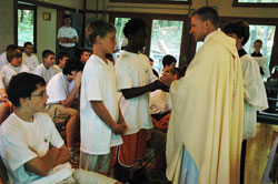 Father Rick Nagel, associate vocations director for the archdiocese, receives offertory gifts from, at left, Patrick Durcholz, a member of Annunciation Parish in Brazil, and Kevin Chambers, a member of Holy Trinity Parish in Indianapolis, during a Mass celebrated on June 14 at Bradford Woods in Morgan County. The Mass was part of Bishop Brut&eacute; Days, a retreat focused on the priesthood that was sponsored by the Bishop Brut&eacute; College Seminary at Marian College in Indianapolis. (File photo/Sean Gallagher) 