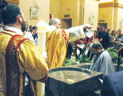 Benedictine Father Julian Peters, administrator pro-tem of SS. Peter and Paul Cathedral Parish in Indianapolis, baptizes Scott Warpool during Cathedral Parish&rsquo;s Easter Vigil on March 22. Transitional Deacon Aaron Jenkins, holding the parish&rsquo;s Easter candle, stands at left. (Photo by Sean Gallagher)
