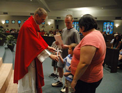 Father Rick Nagel presents a crucifix to Joshua Brown during a Sept. 14 Mass celebrated at Our Lady of the Greenwood Church in Greenwood during the opening weekend of the Parish Vocations Cross Initiative. Joshua received the crucifix on behalf of his parents, Jennifer and Brian Brown, and his brother, Marcus. The cross initiative is sponsored by the archdiocesan Office of Priestly and Religious Vocations. Father Nagel is Our Lady of the Greenwood&rsquo;s associate pastor and the associate director of archdiocesan vocations. (Photo by Sean Gallagher) 