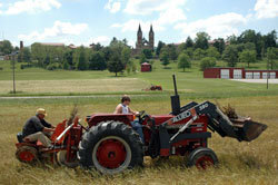 Farmers work in a field in Spencer County. Saint Meinrad Archabbey&rsquo;s Church of Our Lady of Einseideln is visible in the distance. Rural parishes like nearby St. Meinrad Parish in St. Meinrad and others throughout the Archdiocese of Indianapolis offer a unique connection of faith and family. (Photo by John Farless)