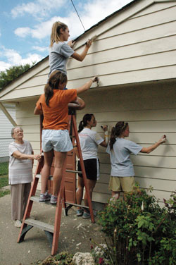 Senior citizen Pansy Mitchell of Indianapolis watches members of Roncalli High School&rsquo;s varsity volleyball team paint her faded garage on Sept. 27 during the ninth&nbsp;annual Angels&nbsp;from the Heart community service project coordinated by Sacred Heart of Jesus Parish. The service program was organized in&nbsp;2000 to celebrate&nbsp;the 125th&nbsp;anniversary of the founding of Sacred Heart Parish in 1875 on the near-south side of the city. (Photo by Mary Ann Wyand) 