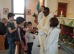 Father Dominic Chukwudi receives offertory gifts from Amanda Tovey, left, C. J. Murrary, Virginia Graf and Jacob Bray during a Nov. 9 Mass at Holy&nbsp;Rosary Church in Seelyville. Assisting Father Chukwudi are altar servers Sara Baugh, left, and Molly Tovey. A priest of the Diocese of Issele-Uku, Nigeria, Father Chukwudi has ministered in the archdiocese since 2006 and is currently the administrator of Annunciation Parish in Brazil and Holy&nbsp;Rosary Parish in Seelyville. (Photo by Sean Gallagher) 