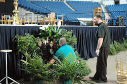 Father Aaron Jenkins works on art and environment details for the stage on May 2 at Lucas Oil Stadium in Indianapolis in preparation for the archdiocese&rsquo;s 175th anniversary Mass there on May 3. He is the associate pastor of Holy Name of Jesus Parish in Beech Grove and the chaplain of Father&nbsp;Thomas Scecina Memorial High School in Indianapolis. A group of Scecina Memorial students helped him move the liturgical furniture onto the stage. (Photo by Mary Ann Wyand) 
