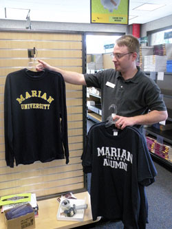 Zack Fincher, Marian University Bookstore supervisor, removes the last three T-shirts with &ldquo;Marian College&rdquo; printed on them and replaces them with &ldquo;Marian University&rdquo; T-shirts. All &ldquo;Marian College&rdquo; items were on sale for 75 percent off the original price. &ldquo;These [Marian College T-shirts] are pretty much all that&rsquo;s left,&rdquo; Fincher said. (Photo by Kamilla Benko) 
