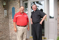 Frank Wiseman Jr. and Father Michael Hilderbrand, pastor of St. Mary Parish in Lanesville, stand together in front of Wiseman&rsquo;s house in Floyds Knobs on July 30. The house is built on the same site where, 19 years ago, Wiseman&rsquo;s previous house was destroyed by a tornado. Later that same day, Father Hilderbrand prayed with Wiseman, a member of St. Mary-of-the-Knobs Parish in Floyd County, and helped him contact family members who were away from home. (Submitted photo)