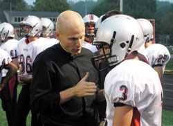 After a play during a football game against Park Tuder School on Sept. 25, Father John Hollowell shares a coaching moment with Eddie Cmehil, a sophomore wide receiver and defensive back for Cardinal Ritter&rsquo;s varsity football team. (Photo by John Shaughnessy)