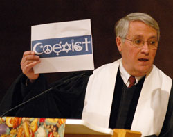 Dr. Robert Welsh, the president of the Council on Christian Unity of the Indianapolis-based Christian Church (Disciples of Christ), holds up an image of a bumper sticker which uses religious symbols to spell the word &ldquo;coexist&rdquo; to invite those in attendance to consider that the various world faith traditions are called to&nbsp;more than coexistence, but also to build community. (Photo by Sean Gallagher)