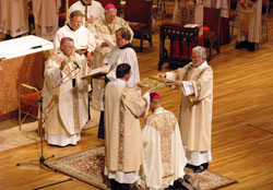 Archbishop Charles J. Chaput of Denver prays a prayer of consecration over a kneeling Bishop-designate Paul D. Etienne during a Dec. 9 episcopal ordination and installation liturgy at the Cheyenne Civic Center in Cheyenne Wyo. Deacons Tim Martinson, from left, and Doug Vlchek, both of the Cheyenne&nbsp;Diocese, hold a Book of the Gospels over Bishop-designate Etienne&rsquo;s head, which, among other things, symbolizes the yoke that Christ invited his followers to take upon themselves. (Photo by Sean Gallagher)