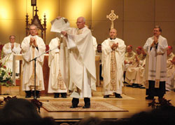 During the Dec. 9 episcopal ordination and installation of Bishop Paul D. Etienne in the Cheyenne Civic Center in Cheyenne, Wyo., Father Michael Carr, vicar general of the Cheyenne Diocese, holds the apostolic letter from Pope&nbsp;Benedict XVI in which the pontiff appointed Bishop&nbsp;Etienne to lead the Church in Wyoming. Standing behind Father Carr applauding are Fathers Carl Gallinger, left, James Heiser and Thomas Cronkleton, all priests of the Cheyenne Diocese and members of its college of consultors. (Photo by Sean Gallagher)