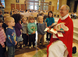 Father Robert Gilday, right, receives a spiritual bouquet from Canaan Miller, from left, Gabrielle Herner, Gavin Turner, Lily Russell, Mira Jackson and Shelby Robinett, all preschool students at Little Flower School in Indianapolis, during a Feb. 5 Mass at the parish church. Father Gilday is the pastor of St.&nbsp;Therese of the Infant Jesus (Little Flower) Parish. (Photo by Sean Gallagher)