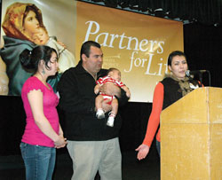 Mariana Ruiz, right, speaks as a translator for her uncle and Gabriel Project volunteer, Luis Aguayo, second from left during a March 23 Gabriel Project fundraising banquet in Indianapolis. Aguayo is holding Emil Lopez, the son of Maria&nbsp;Lopez, left. Emil was saved from abortion through the assistance of Aguayo and other Gabriel Project volunteers. (Photo by Sean Gallagher)