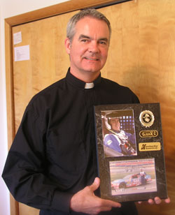 Standing in his office, Father John Meyer holds a plaque that celebrates one of the most unusual adventures that he&rsquo;s had during his 28 years as a priest in the archdiocese&mdash;driving up to 150 mph at the Kentucky Speedway while participating in the Richard Petty Driving School. The experience was a gift from one of the two parishes he leads in southern Indiana. (Photo by John Shaughnessy)