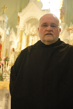 Benedictine Father Barnabas Gillespie stands in front of the altar at St. Pius V Church in Troy. He serves as the pastor of that parish and St. Michael Parish in Cannelton, and provides sacramental assistance at St. Paul Parish in Tell&nbsp;City and St. Mark Parish in Perry County. (Photo by Sean Gallagher)