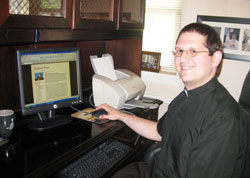 Father Eric Augenstein, pastor of Our Lady of Perpetual Help Parish in New Albany, sits at his computer in the parish office on July 7. On his blog, &ldquo;Perpetual Priest,&rdquo; Father Augenstein posts the text of his weekend homilies, thus widening the reach of his ministry. (Submitted photo)