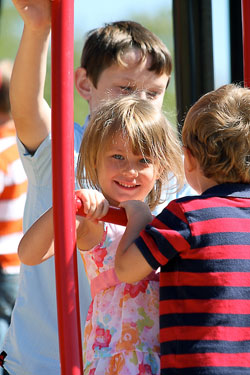Surrounded by her brothers, Grace McVey flashes a smile as she plays on the new playground equipment that was recently dedicated at St. Charles Borromeo Parish in Bloomington in honor of the late pastor, Father&nbsp;Charles Chesebrough. Justin Dyer stands behind Grace while Liam McVey faces his sister. The three children of Robert and Marie McVey attend St. Charles Borromeo School. (Submitted photo)