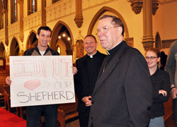 Archbishop Daniel M. Buechlein talks with Indiana University-Purdue University Indianapolis senior Michael Conner, left, of St. Paul Parish in Tell City, who holds a sign praising Archbishop Buechlein after the Jan. 14 press conference at St. John the Evangelist Church in Indianapolis. Father Rick Nagel, center, the director of the archdiocesan Office of Young Adult and College Campus Ministry, also talked with the archbishop and students after Bishop-designate Christopher J. Coyne&rsquo;s official introduction. (Photo by Mary Ann Wyand)