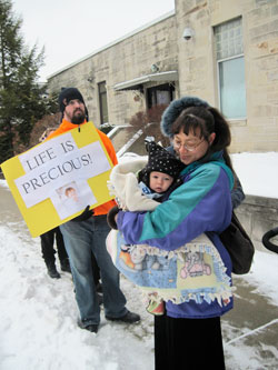 Cindy Lee holds her 5-month-old son, Simon, as she prays outside the Planned Parenthood clinic in Bloomington during the March for Life on Jan. 24. They are members of St. Paul Catholic Center in Bloomington. Holding the poster is Patrick&nbsp;Faulkenberg, a member of St. John the Apostle Parish. (Photo by Kamilla Benko)