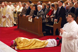 Bishop Christopher J. Coyne, the new auxiliary bishop of the Archdiocese of Indianapolis, lays prostrate in prayer on March 2 before the altar and sanctuary at St. John the Evangelist Church in Indianapolis during the praying of the Litany of the Saints as part of his episcopal ordination Mass. His mother, Rita Coyne of Woburn, Mass., center, and other members of his family kneel in prayer in the pews behind him. Bishop Coyne&rsquo;s posture is a prayerful sign of humility before God and obedience to the ministry that he has been called by Pope Benedict XVI to serve the Catholic Church in central and southern Indiana. Seminarian Jerry Byrd, a member of St. Louis Parish in Batesville, is shown to the right of Bishop Coyne. (Photo by Sean Gallagher)