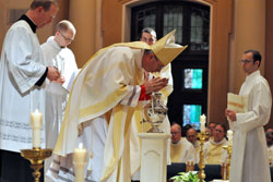 Bishop Christopher J. Coyne, the auxiliary bishop and vicar general, ritually breathes on chrism oil that he then blessed on April 19 during the archdiocese&rsquo;s annual chrism Mass at SS. Peter and Paul Cathedral in Indianapolis. Assisting Bishop Coyne are, from left, Father Patrick Beidelman, seminarian David Marcotte, transitional Deacon Dustin Boehm (partially obscured) and seminarian Michael Keucher. (Photos by Sean Gallagher)