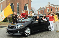 Father Jonathan Meyer, pastor of St. Mary, St. Ann and St. Joseph parishes in Jennings County, sits&nbsp;behind the wheel of his 2009 Toyota Corolla, which he is giving away to raise funds to help nine young adults attend World Youth Day on Aug. 16-21 in Madrid, Spain. Six young adults from Jennings County parishes posing with Father Meyer to promote the fundraiser are, from left, Danny Capes, Kelly Ertel, Charlotte Leach, Amber Andrews, Laura Coons and Kate Eder. Capes, Ertel, Leach, Coons and Eder are among the World Youth Day pilgrims. (Submitted photo)
