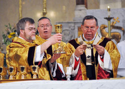 Assisting Archbishop Daniel M. Buechlein, right, Deacon Kerry Blandford, left, elevates the chalice during the doxology of the eucharistic prayer during the March 2 episcopal ordination of Bishop&nbsp;Christopher J. Coyne, center, at St. John the Evangelist Church in Indianapolis. (File photo by Mary Ann Wyand)