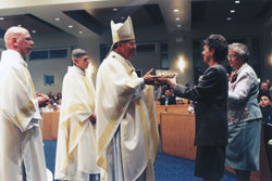 Archbishop Daniel M. Buechlein accepts offertory gifts from Beverly Hansberry and Franciscan Sister Yvonne Conrad at the Dec. 1, 2001, dedication Mass for the new St. Simon the Apostle Church in Indianapolis. Transitional Deacon John McCaslin, left, a St. Simon parishioner who was ordained to the priesthood in June 2002, and Father Robert Sims, then St. Simon&rsquo;s pastor, assisted the archbishop during the liturgy. At the time, Hansberry was St. Simon&rsquo;s director of faith formation, and Sister Yvonne was the parish&rsquo;s administrative assistant. (File photo by Mary Ann Wyand)