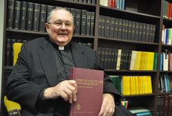 Msgr. Frederick Easton, now adjunct vicar judicial, holds a copy of the Code of Canon Law while sitting in a conference room of the archdiocese&rsquo;s Metropolitan Tribunal in the Archbishop Edward T. O&rsquo;Meara Catholic Center in Indianapolis on Oct. 6. Msgr. Easton led the tribunal as its vicar judicial for 31 years before retiring in July. (Photo by Sean Gallagher)