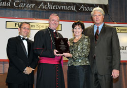 Bishop Christopher J. Coyne presents an award for Archbishop Emeritus Daniel M. Buechlein to his niece, Anne Wilmes, during the Celebrating Catholic School Values Awards Dinner on Oct. 26. The award recognized the archbishop for making Catholic education a priority during his 19-year tenure as the spiritual leader of the archdiocese. The archbishop was unable to attend the dinner. Also in the photo are, left, Harry Plummer, executive director of Catholic education and faith formation for the archdiocese, and Art Wilmes, Anne&rsquo;s husband. (Photo by Rob Banayote)