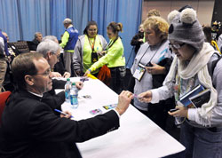 Bishop Charles C. Thompson of Evansville, Ind., left, gives a signed trading card of himself to Catherine Nguyen of New Orleans on Nov. 18 in the National Catholic Youth Conference&rsquo;s thematic park at the Indiana Convention Center in Indianapolis. (Photo by Sean Gallagher)
