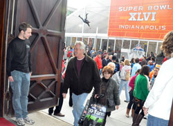 As a zip line rider zooms over thousands of pedestrians filling Capitol Avenue, Keith Echternach, left, a member of St. John the Evangelist Parish in Indianapolis, welcomes Super Bowl visitors into his parish&rsquo;s historic church on Feb. 3. (Photo by Sean Gallagher)