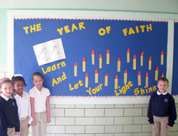 Amelia Harrigan, left, Meredith Attai, Hailey Kocher and Gavin&nbsp;Farris, all second-grade students at St. Roch School in Indianapolis, pose on Jan. 15 in front of a bulletin board at their school dedicated to the Year of Faith. Each student wrote a way to evangelize on the bulletin board candles. Answers included, &ldquo;I will give food to the poor,&rdquo; and &ldquo;I will proclaim the word to others.&rdquo; (Submitted photo)