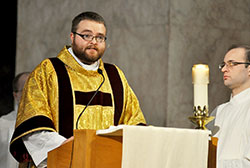 Transitional Deacon Doug Marcotte proclaims the Gospel during the archdiocese&rsquo;s annual chrism Mass on March 26 at SS. Peter and Paul Cathedral in Indianapolis. He will be ordained to the priesthood on May 18. Seminarian Michael Keucher holds a candle at right. (Submitted photo/Kent Hughes)