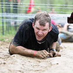 Father Jonathan Meyer crawls beneath barbed wire during the Spartan Race in Laurel on April 27, 2012. The barbed wire challenge will be part of the &ldquo;Tame the Terrain&rdquo; race in North Vernon on June 22. The event is a fundraiser to benefit young adults and teenagers who are members of St. Mary Parish in North Vernon, and St. Ann and St. Joseph parishes in Jennings County. (Submitted photo)