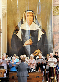 Members of the Sisters of Providence choir, joined by the Saint Mary-of-the-Woods College Chorale, sing during the Mass celebrating the feast of St. Theodora at the Church of the Immaculate Conception in St. Mary-of-the-Woods on Oct. 3. The wooden box in front of the choir director contains the remains of St. Theodora, and the hanging banner was the one displayed in St. Peter&rsquo;s Square at the Vatican when the founder of the Sisters of Providence was beatified in 1998. (Photo by Natalie Hoefer)