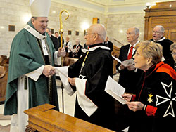 Archbishop Joseph W. Tobin stops to shake hands with Dr. Hans Geisler during the opening procession of an Oct. 14 Mass in the Blessed Sacrament Chapel of SS. Peter and Paul Cathedral in Indianapolis. The Mass celebrated the 900th anniversary of the formal founding of the Order of Malta, an order of lay Catholics that serves the sick, disabled and people in need. Geisler and his wife, Margie, right, are wearing the order&rsquo;s habit. They are members of St. Luke the Evangelist Parish in Indianapolis. Also attending the Mass and standing behind Geisler are John Fink, editor emeritus of The Criterion, and George Maley, a member of the order. (Photo by Sean Gallagher)