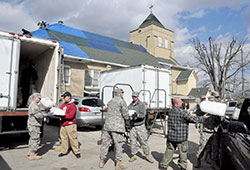 Members of the Indiana National Guard and other rescue workers load ice on March 3, 2012, into a refrigerated truck parked next to St. Francis Xavier Church in Henryville, Ind., while workers attach a tarp to the church&rsquo;s damaged roof that resulted from a tornado the previous day. Archdiocesan Catholics were generous in helping those affected by the storm, raising nearly $250,000 in a special collection. (File photo by Sean Gallagher)