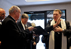 Archbishop Joseph W. Tobin blesses the people and studios at Catholic Radio Indy&rsquo;s new offices on Dec. 17, while Msgr. Joseph Schaedel, pastor of St. Luke the Evangelist Parish in Indianapolis, holds the prayer book, and Catholic Radio Indy founder and chairman Bob Teipen, middle, bows his head in prayer. 