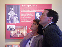 Mary Ritter and Paul Scales study a display in a museum room now located in the restored birthplace and boyhood home of Cardinal Joseph E. Ritter in New Albany on March 13. They traveled from Cincinnati to hear Louisville Archbishop Joseph Kurtz and see the restoration of Mary Ritter&rsquo;s great-uncle&rsquo;s New Albany childhood home. A portrait of Cardinal Ritter graces the wall behind them. (Photo by Patricia Happel Cornwell)