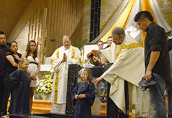 Bailey Wilson is baptized by Father Eric Johnson, pastor at Our Lady of Perpetual Help Parish in New Albany, during the Easter Vigil at the parish&rsquo;s church on April 19. Deacon Jeffrey Powell assists Father Johnson. (Submitted photo by Crit Fisher)