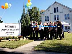 In New Albany, St. Elizabeth Catholic Charities agency director Mark Casper, third from left in the front row, cuts a ribbon on Oct. 10, 2013, marking the official opening of the agency&rsquo;s new administration and social services building. Built in 1850 as the rectory for the former Holy Trinity Parish, the structure&rsquo;s historic preservation and restoration was completed during the last week of June. New Albany Mayor Jeff Gahan holds the ribbon at left. (Submitted photo)