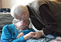 In this photo from June 2012, St. Augustine Home for the Aged resident Donald Bird of Indianapolis kisses his wife, Mary, in her room at the home operated by the Little Sisters of the Poor. A conference being held on Oct. 17 at the Archbishop Edward T. O&rsquo;Meara Catholic Center in Indianapolis will address practical, legal and ethical issues that caregivers often face. (Criterion file photo)