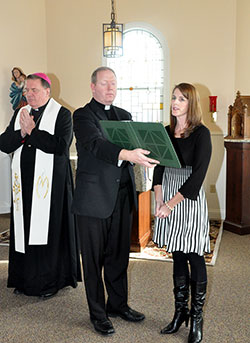 Archbishop Joseph W. Tobin listens as Sarah Bardol, director of the new Women&rsquo;s Care Center in Indianapolis, reads in the chapel during a service to bless the facility on Nov. 19. Father Patrick Beidelman, executive director of the archdiocesan Secretariat for Spiritual Life and Worship, holds a book for Bardol. (Photo by Natalie Hoefer)
