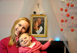 Jennifer Trapuzzano snuggles with her daughter Cecilia in the bedroom where Cecilia sleeps in a crib beneath a crucifix and a photo of her parents. Cecilia was born on April 25, 2014&mdash;24 days after her father Nathan Trapuzzano was shot and killed during a robbery as he took a walk through their Indianapolis neighborhood. (Photo by John Shaughnessy)