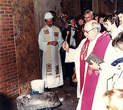 With members of St. Barnabas Parish looking on, Father John Sciarra blesses with holy water the cornerstone for the Indianapolis South Deanery&rsquo;s church in 1985. For the first 20 years of its history, St. Barnabas, like many archdiocesan parishes founded during the baby-boom generation, had Masses celebrated in its school gymnasium. Father Sciarra, St. Barnabas&rsquo; founding pastor, retired in 1989. At left is Father Michael Fritsch, associate pastor of St. Barnabas at the time. (Submitted photo)
