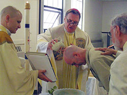 Archbishop Joseph W. Tobin baptizes Frank Wederzak during an April 22 Mass at the Putnamville Correctional Facility in Putnamville. Wederzak is an inmate at the prison. He and five other inmates were baptized and received into the full communion of the Church. Father John Hollowell, left, chaplain at the facility and pastor of Annunciation Parish in Brazil and St. Paul the Apostle Parish in Greencastle, assists in the rite of baptism. Bernie Batto, right, a member of St. Paul Parish, serves as Wederzak&rsquo;s sponsor. (Submitted photo)